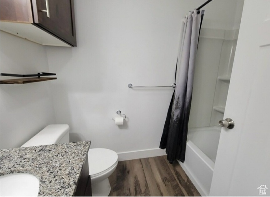 Full bathroom featuring hardwood / wood-style floors, shower / bath combo with shower curtain, vanity, and toilet
