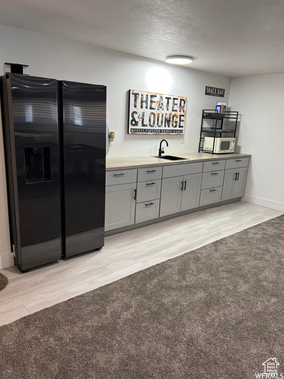 Kitchen featuring black refrigerator with ice dispenser, light hardwood / wood-style flooring, gray cabinets, and sink