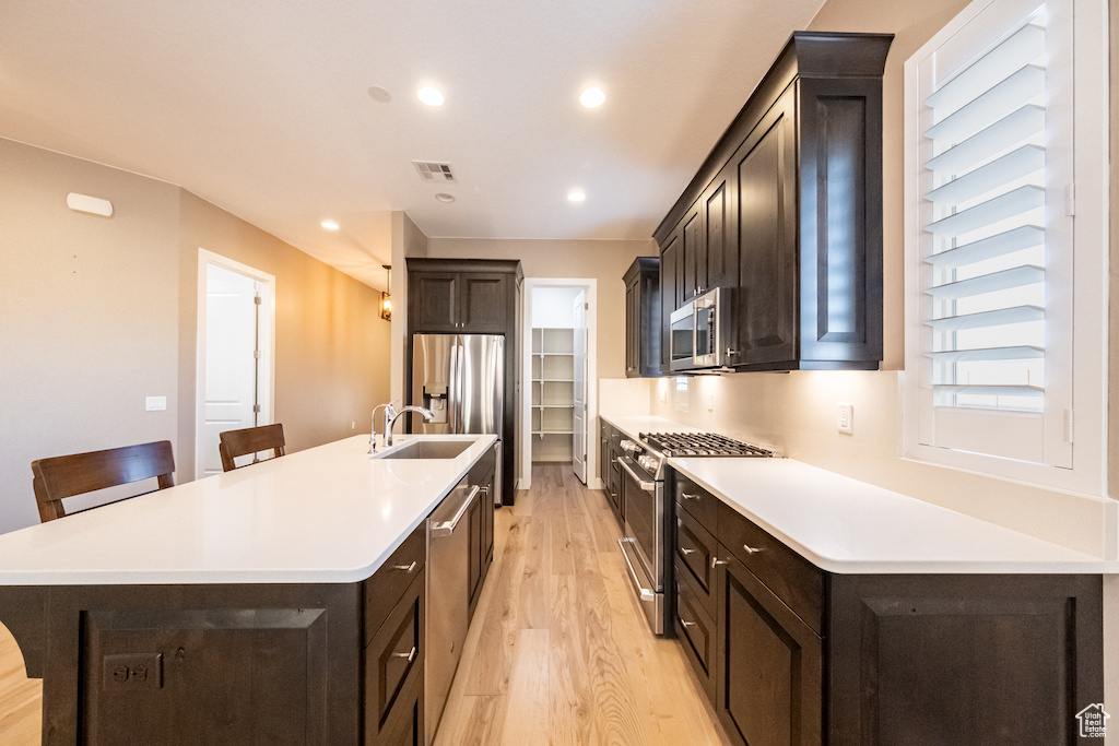 Kitchen featuring a center island with sink, appliances with stainless steel finishes, light hardwood / wood-style flooring, a kitchen breakfast bar, and sink