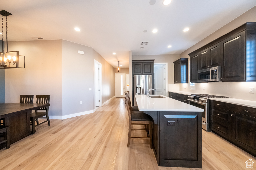 Kitchen featuring light hardwood / wood-style floors, a center island with sink, a notable chandelier, pendant lighting, and appliances with stainless steel finishes