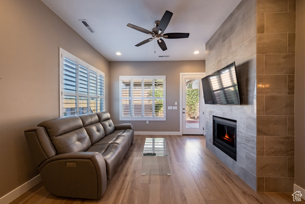 Living room with plenty of natural light, ceiling fan, a tile fireplace, and light wood-type flooring