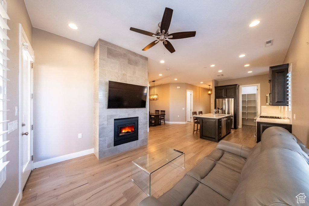 Living room with a fireplace, light hardwood / wood-style flooring, tile walls, and ceiling fan