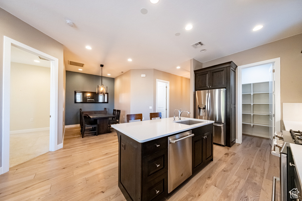 Kitchen featuring light hardwood / wood-style flooring, a center island with sink, hanging light fixtures, sink, and stainless steel appliances