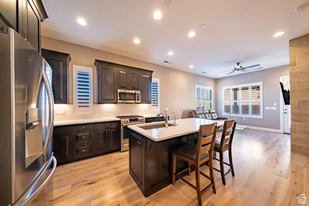 Kitchen with light hardwood / wood-style flooring, a kitchen island with sink, ceiling fan, sink, and appliances with stainless steel finishes