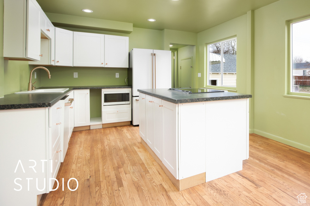 Kitchen featuring white cabinetry, a kitchen island, white appliances, light hardwood / wood-style flooring, and sink