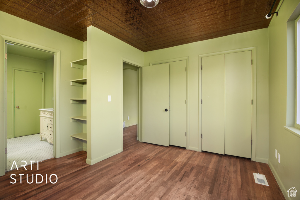 Unfurnished bedroom with two closets, dark wood-type flooring, and ensuite bathroom