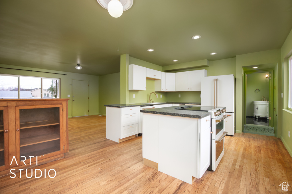 Kitchen featuring light hardwood / wood-style floors, high end appliances, a kitchen island, white cabinetry, and sink