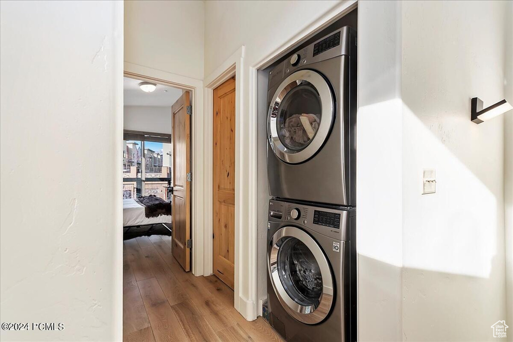Clothes washing area with light hardwood / wood-style floors and stacked washer and clothes dryer
