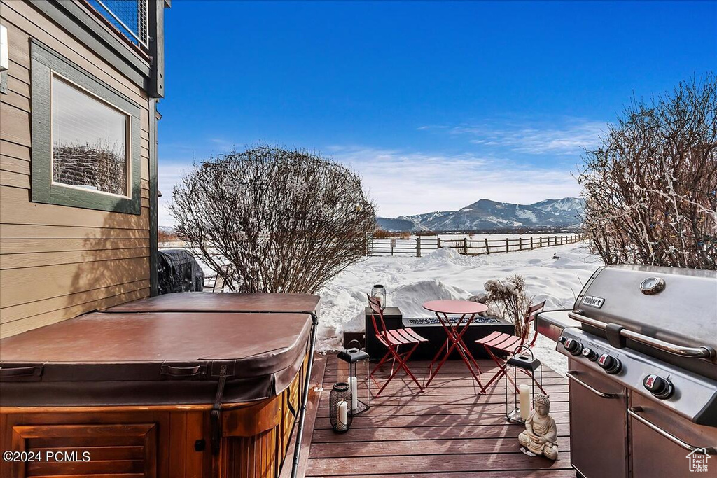 Snow covered deck featuring a mountain view, grilling area, and a hot tub