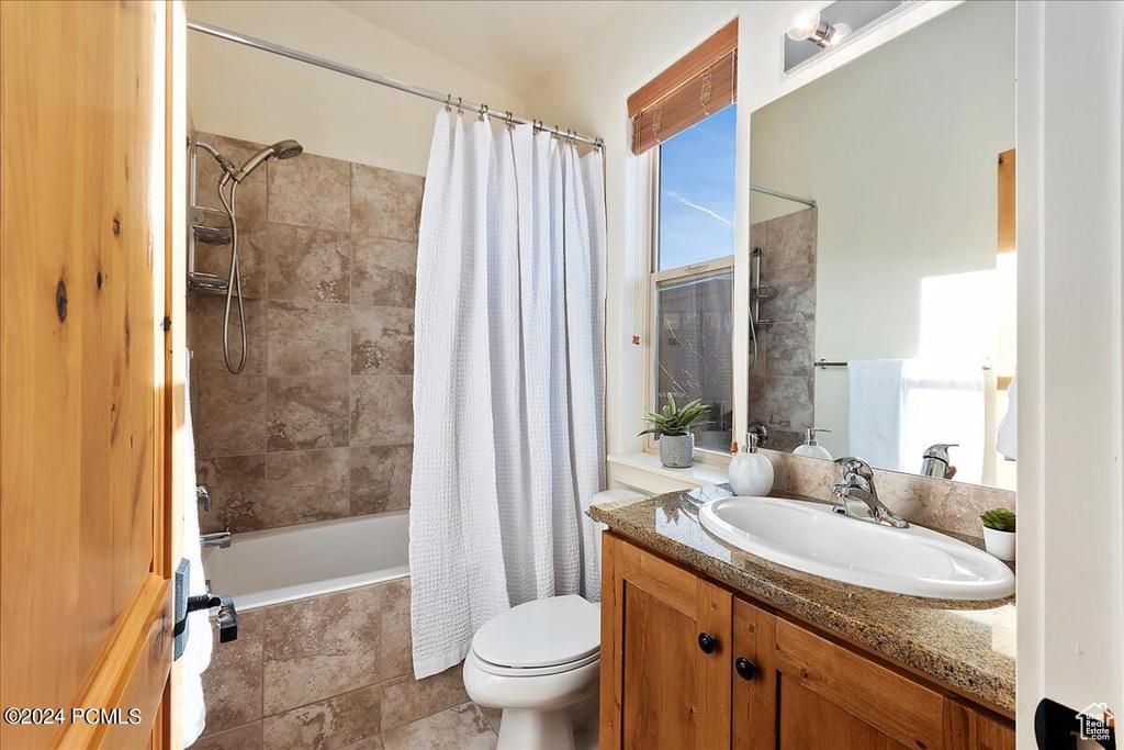 Full bathroom featuring shower / bath combination with curtain, tile floors, vanity with extensive cabinet space, and toilet