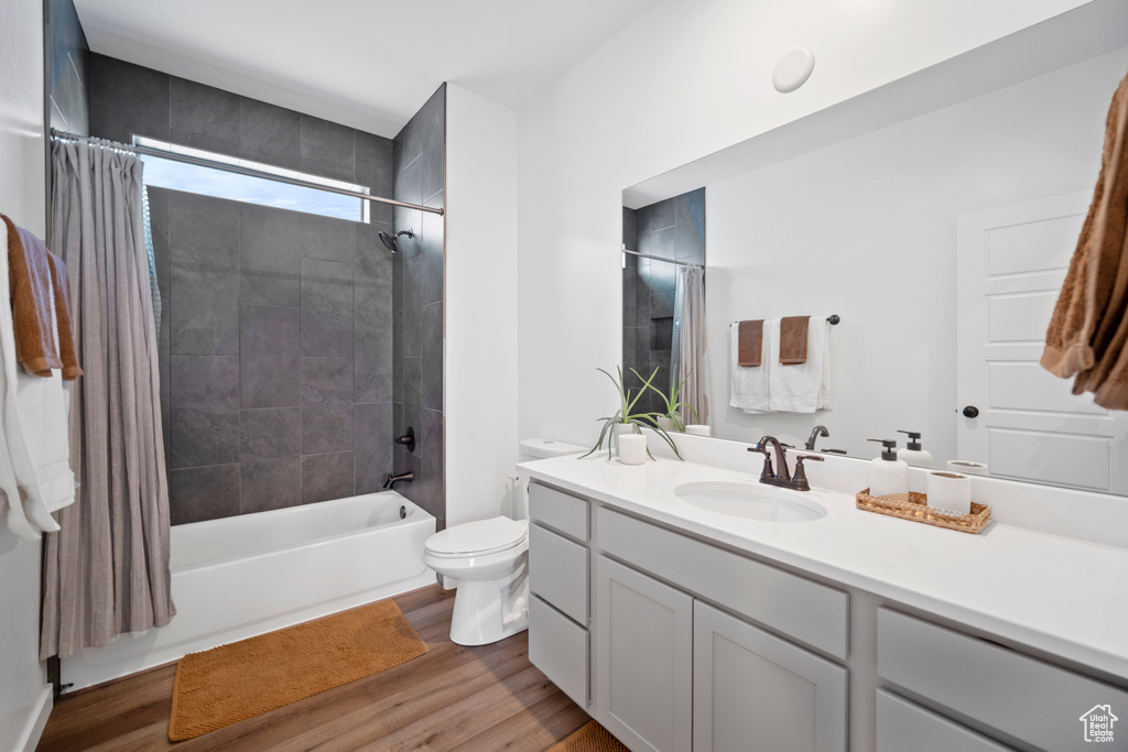 Full bathroom with hardwood / wood-style floors, vanity, shower / tub combo, and toilet