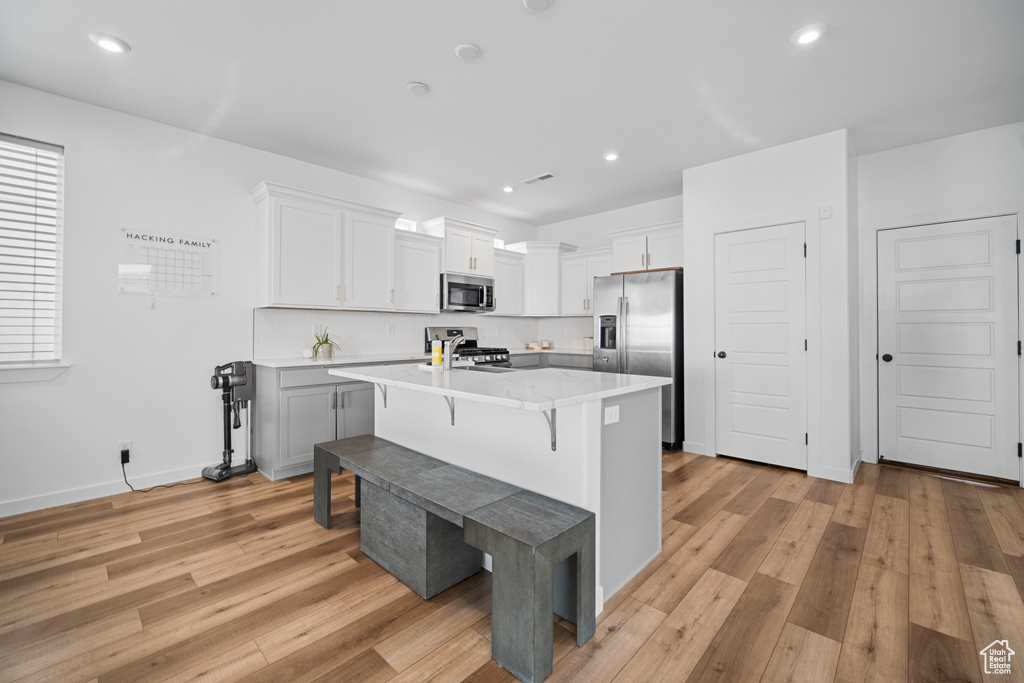Kitchen with light wood-type flooring, stainless steel appliances, white cabinets, a breakfast bar, and a kitchen island with sink