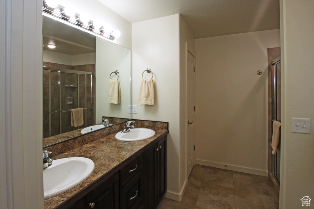 Bathroom featuring a shower with shower door, tile flooring, double sink, and vanity with extensive cabinet space