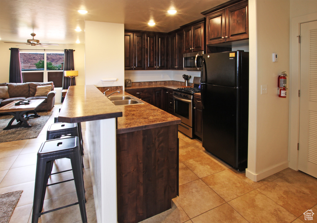 Kitchen with dark brown cabinets, stainless steel appliances, a kitchen breakfast bar, sink, and ceiling fan
