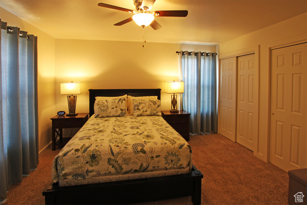 Bedroom with two closets, dark colored carpet, and ceiling fan