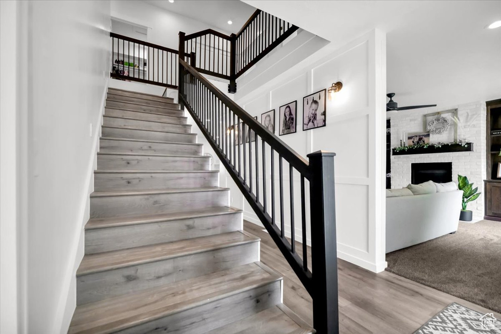 Stairs featuring brick wall, a brick fireplace, ceiling fan, and carpet flooring