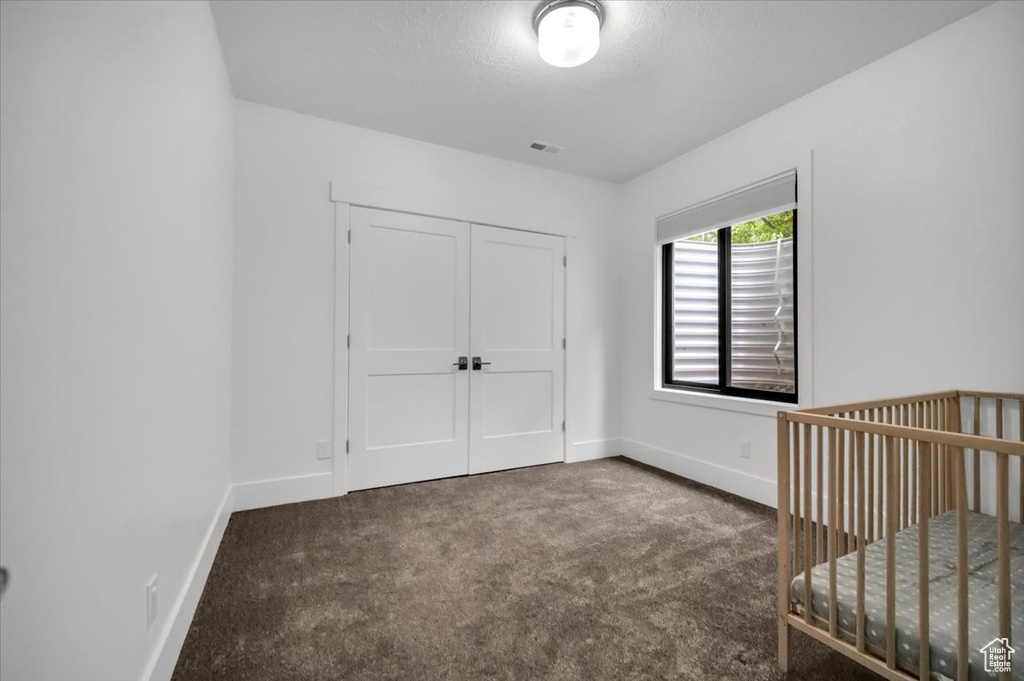 Unfurnished bedroom with a nursery area, dark colored carpet, and a closet