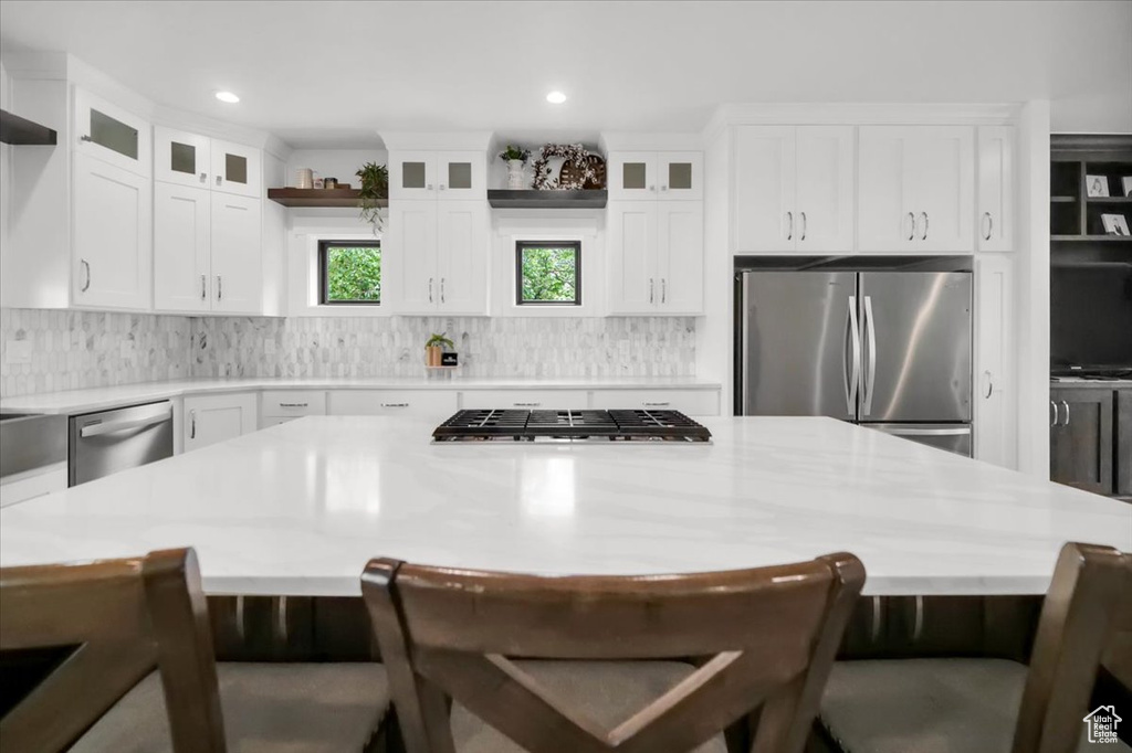 Kitchen featuring a kitchen bar, stainless steel appliances, backsplash, and white cabinets