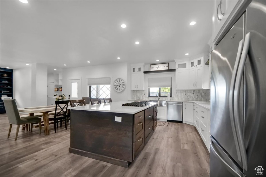 Kitchen featuring light wood-type flooring, white cabinetry, backsplash, appliances with stainless steel finishes, and a center island