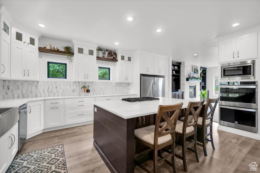 Kitchen featuring a kitchen island, light wood-type flooring, white cabinets, tasteful backsplash, and appliances with stainless steel finishes