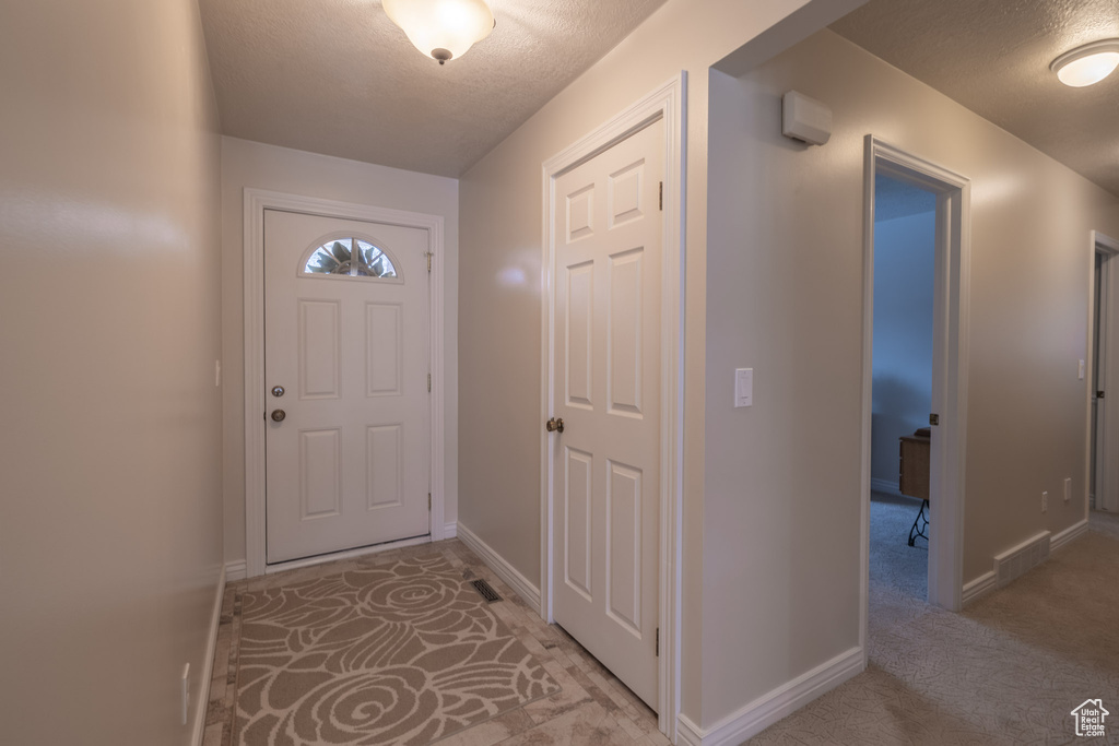 Entryway featuring light colored carpet and a textured ceiling