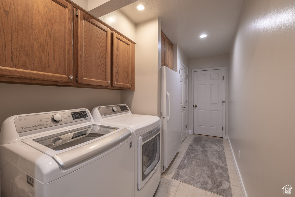 Laundry room with washing machine and clothes dryer, light tile flooring, and cabinets