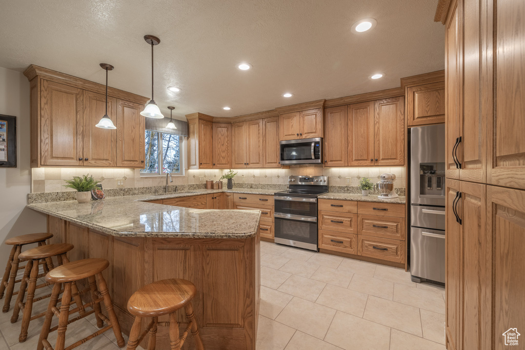 Kitchen with light stone countertops, sink, light tile floors, stainless steel appliances, and pendant lighting