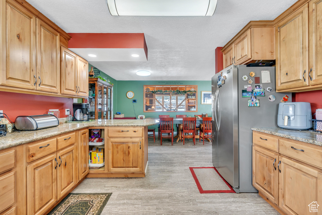 Kitchen featuring stainless steel fridge, light stone countertops, and light wood-type flooring
