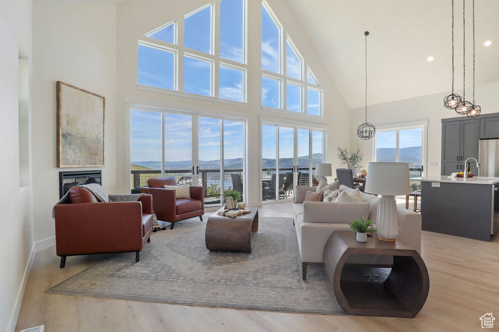 Living room featuring light wood-type flooring, an inviting chandelier, a healthy amount of sunlight, and high vaulted ceiling