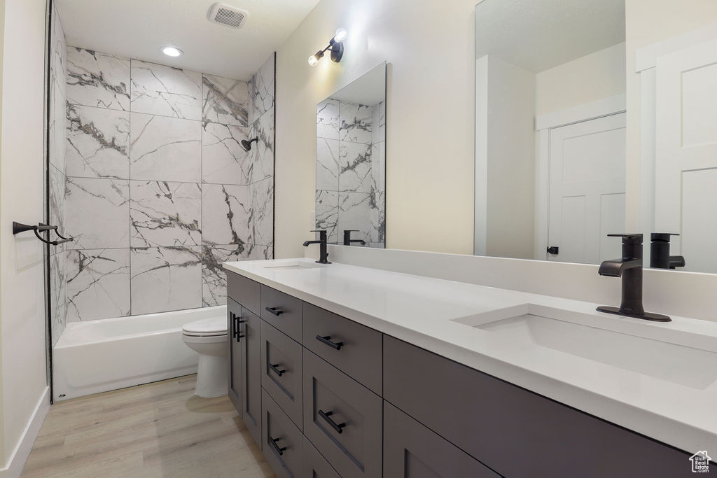 Full bathroom featuring toilet, double vanity, tiled shower / bath, and wood-type flooring