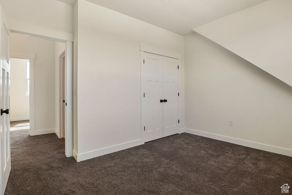 Unfurnished bedroom featuring dark colored carpet, vaulted ceiling, and a closet