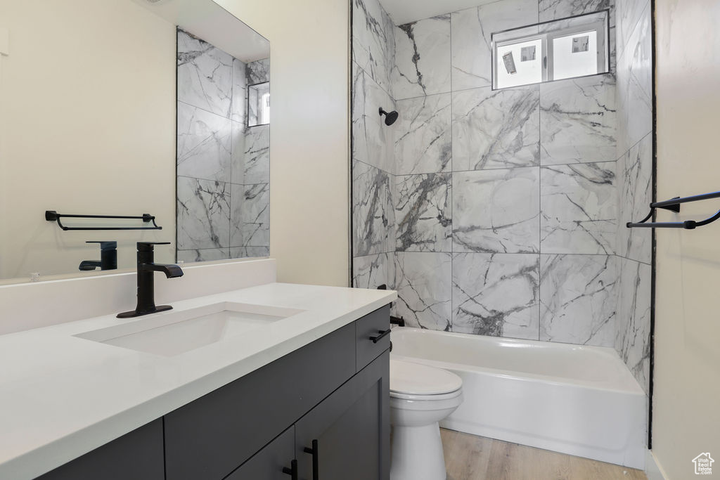 Full bathroom with large vanity, hardwood / wood-style floors, tiled shower / bath combo, and toilet