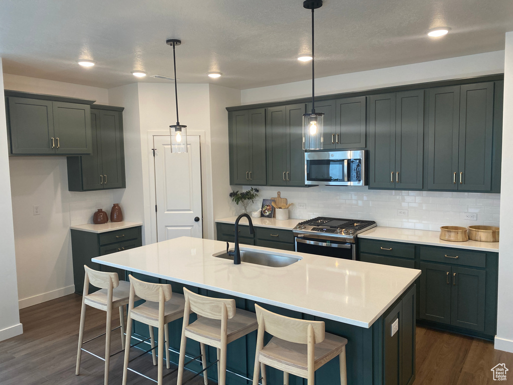 Kitchen featuring decorative light fixtures, dark wood-type flooring, appliances with stainless steel finishes, sink, and a center island with sink