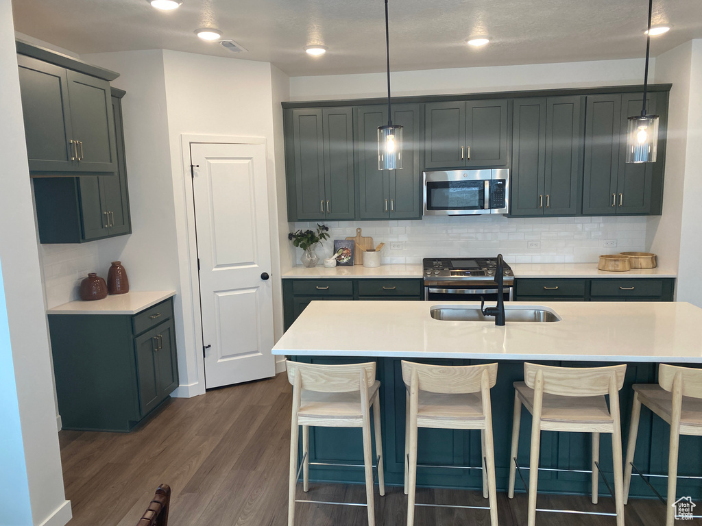 Kitchen featuring sink, dark wood-type flooring, hanging light fixtures, and a center island with sink