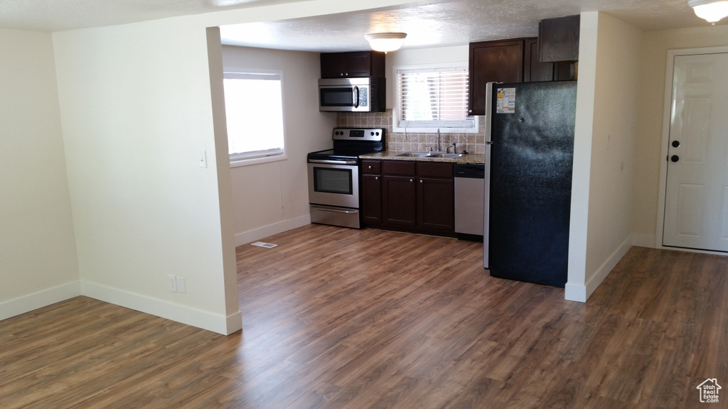 Kitchen featuring backsplash, dark wood-type flooring, dark brown cabinets, sink, and stainless steel appliances