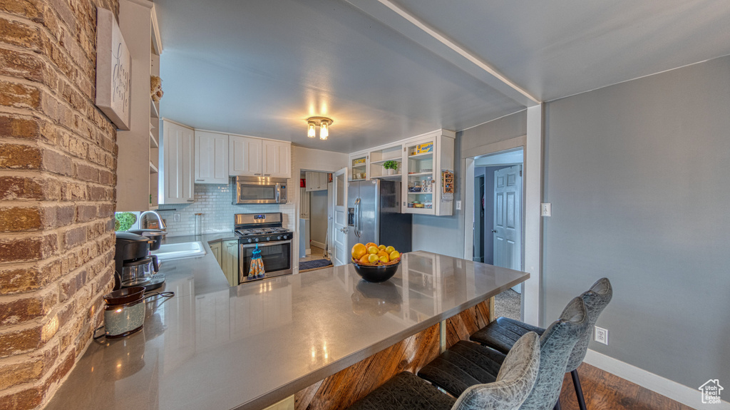 Kitchen with white cabinets, a breakfast bar, tasteful backsplash, appliances with stainless steel finishes, and sink