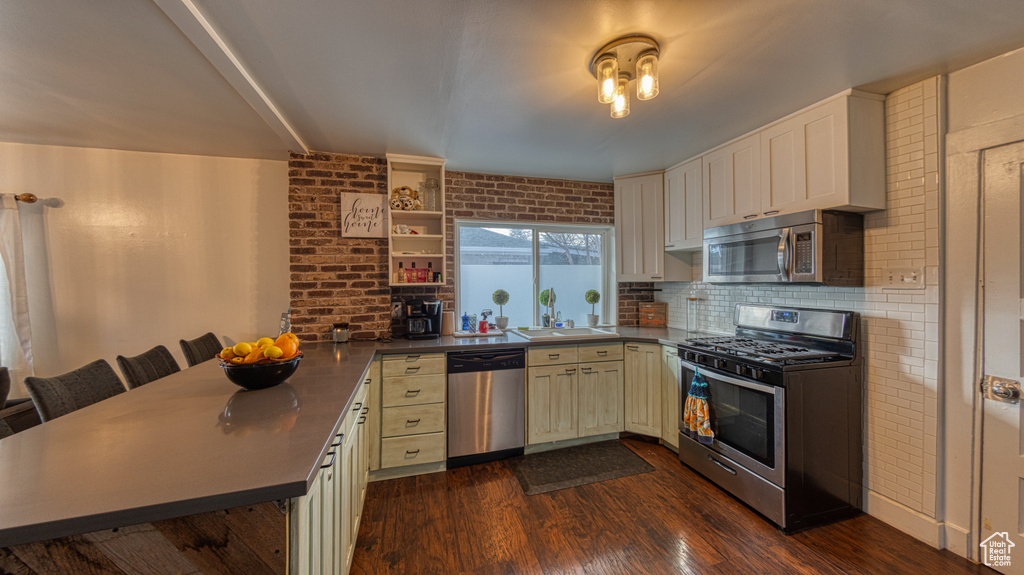 Kitchen with a breakfast bar area, dark hardwood / wood-style floors, sink, stainless steel appliances, and kitchen peninsula