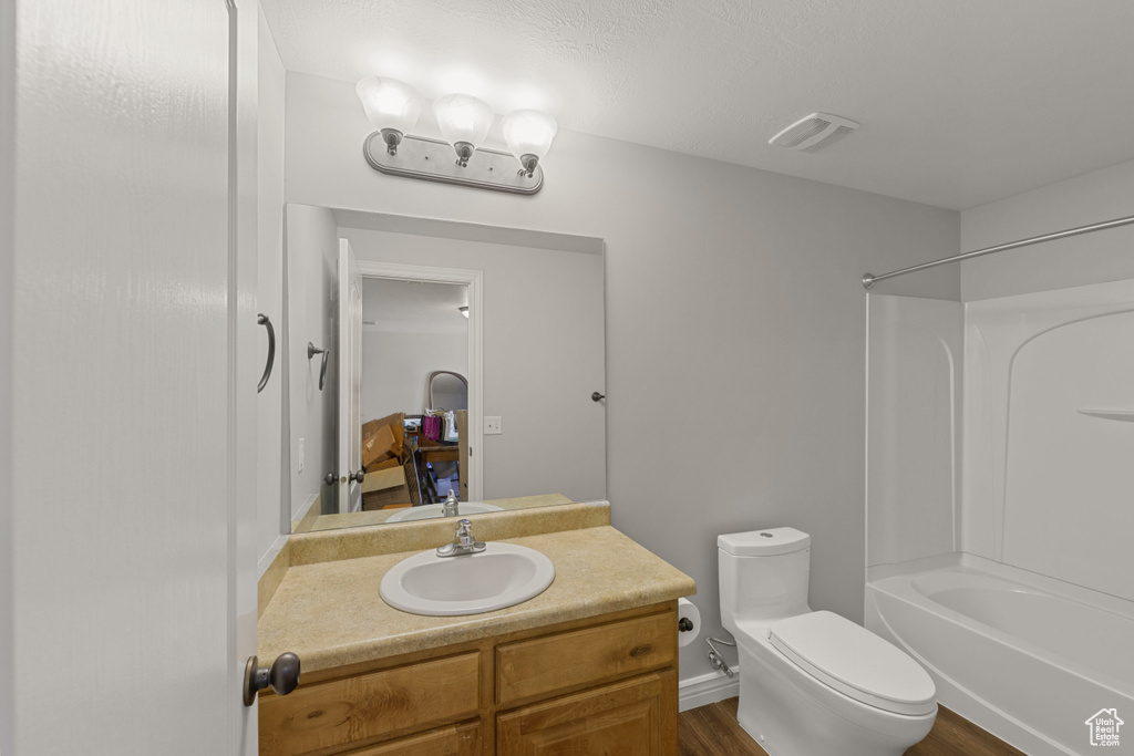 Full bathroom with large vanity, tub / shower combination, toilet, and wood-type flooring