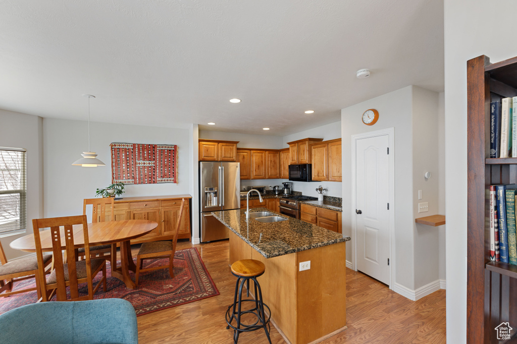 Kitchen with light hardwood / wood-style floors, a center island with sink, a kitchen breakfast bar, high quality appliances, and pendant lighting
