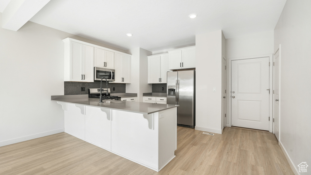 Kitchen with stainless steel appliances, white cabinetry, kitchen peninsula, light hardwood / wood-style floors, and a kitchen breakfast bar