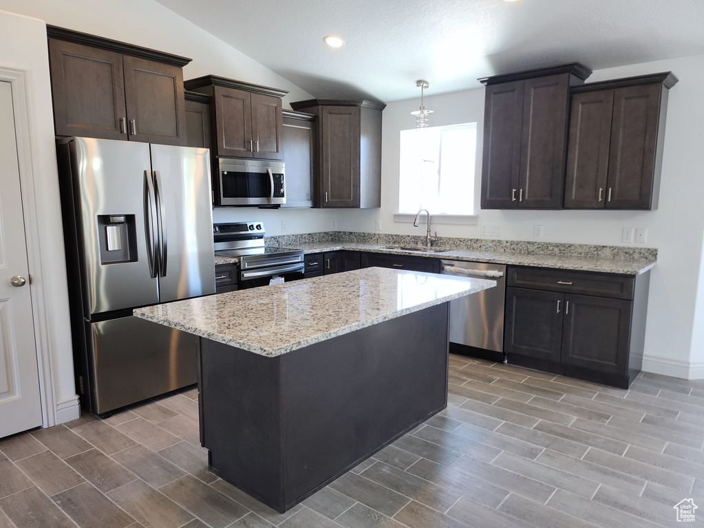 Kitchen featuring decorative light fixtures, light stone countertops, appliances with stainless steel finishes, sink, and a kitchen island