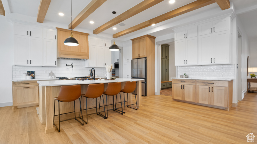 Kitchen with pendant lighting, light hardwood / wood-style floors, a kitchen island with sink, and tasteful backsplash