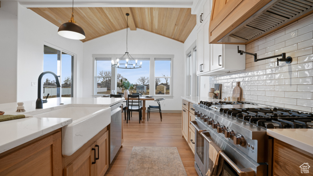 Kitchen featuring a chandelier, custom range hood, tasteful backsplash, appliances with stainless steel finishes, and light hardwood / wood-style floors