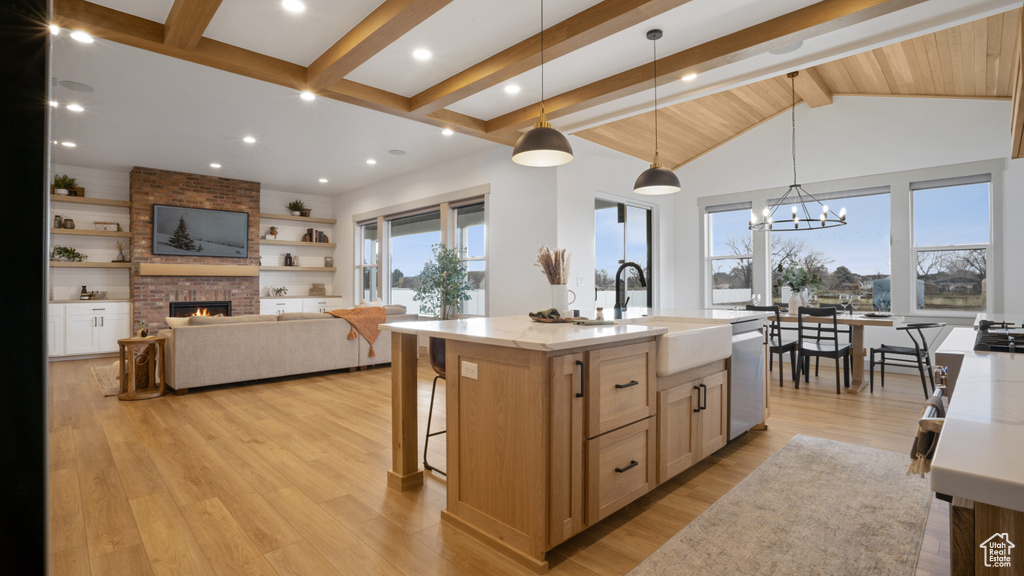 Kitchen featuring a kitchen island with sink, light wood-type flooring, a fireplace, an inviting chandelier, and pendant lighting
