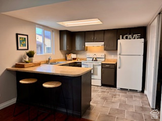 Kitchen featuring white appliances, kitchen peninsula, dark brown cabinets, light tile floors, and sink