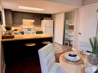 Kitchen featuring fume extractor, kitchen peninsula, light tile flooring, range, and white refrigerator