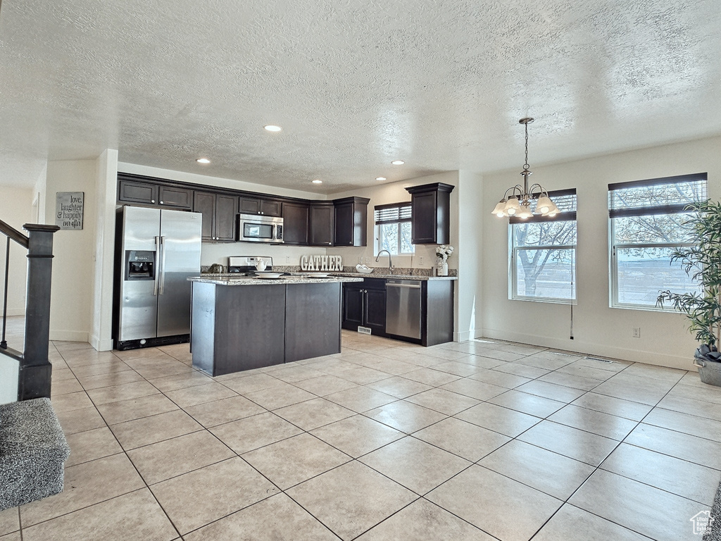 Kitchen with a center island, hanging light fixtures, dark brown cabinets, stainless steel appliances, and light tile floors