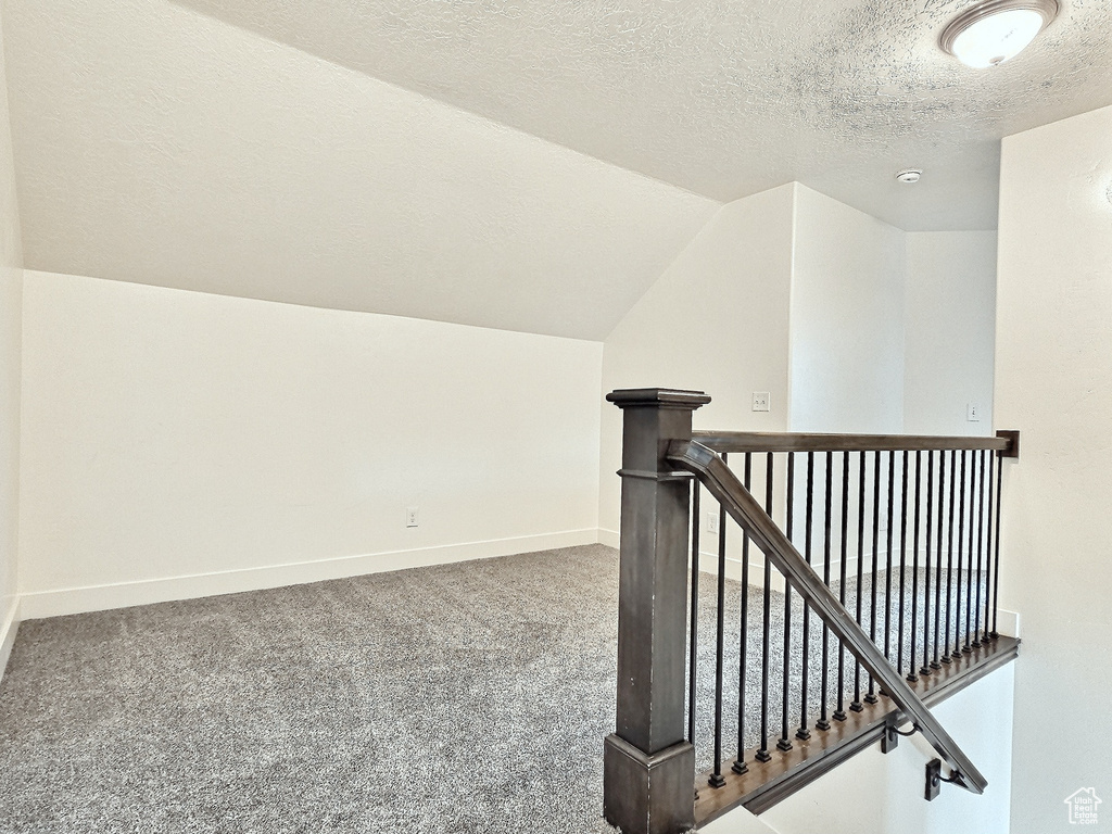 Stairway with vaulted ceiling, a textured ceiling, and carpet floors