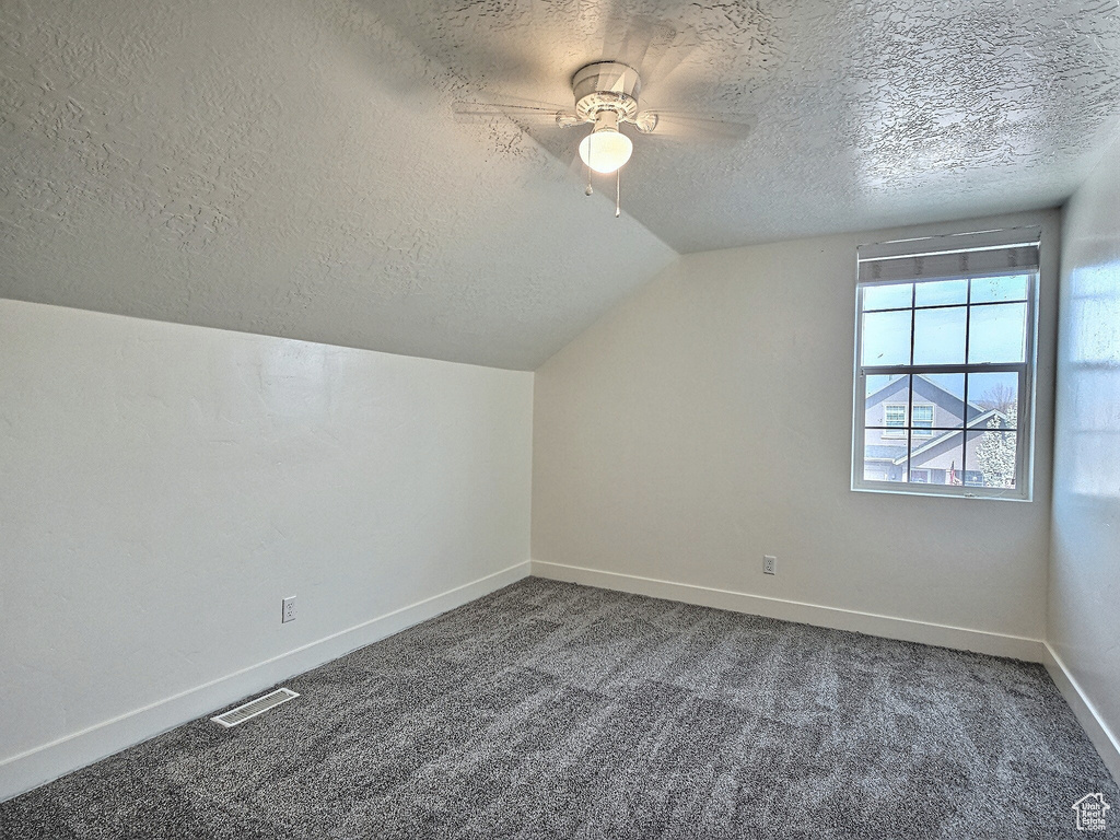 Additional living space with lofted ceiling, ceiling fan, dark carpet, and a textured ceiling