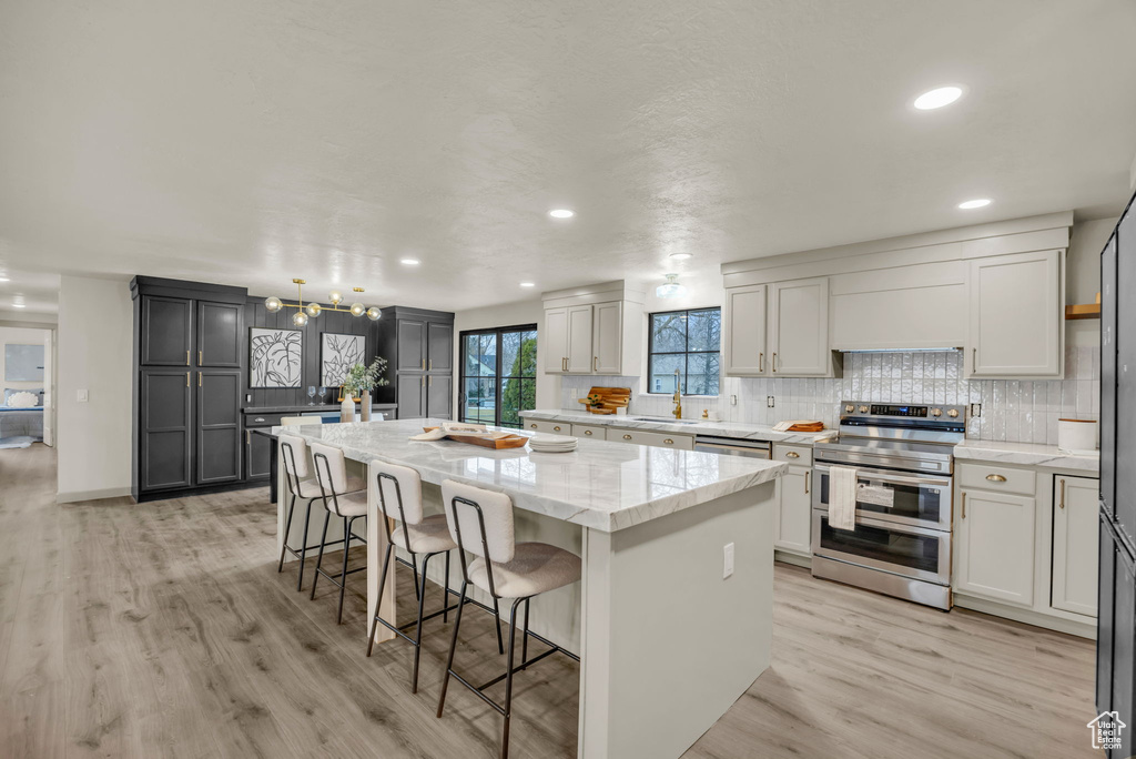 Kitchen featuring stainless steel appliances, light stone countertops, a breakfast bar area, light hardwood / wood-style flooring, and a center island